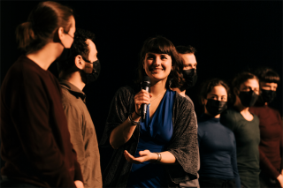 Naila Kuhlman addresses a group of people on stage while holding a microphone