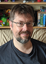 Chris Corkery smiling at the camera, seated in front of a bookcase.