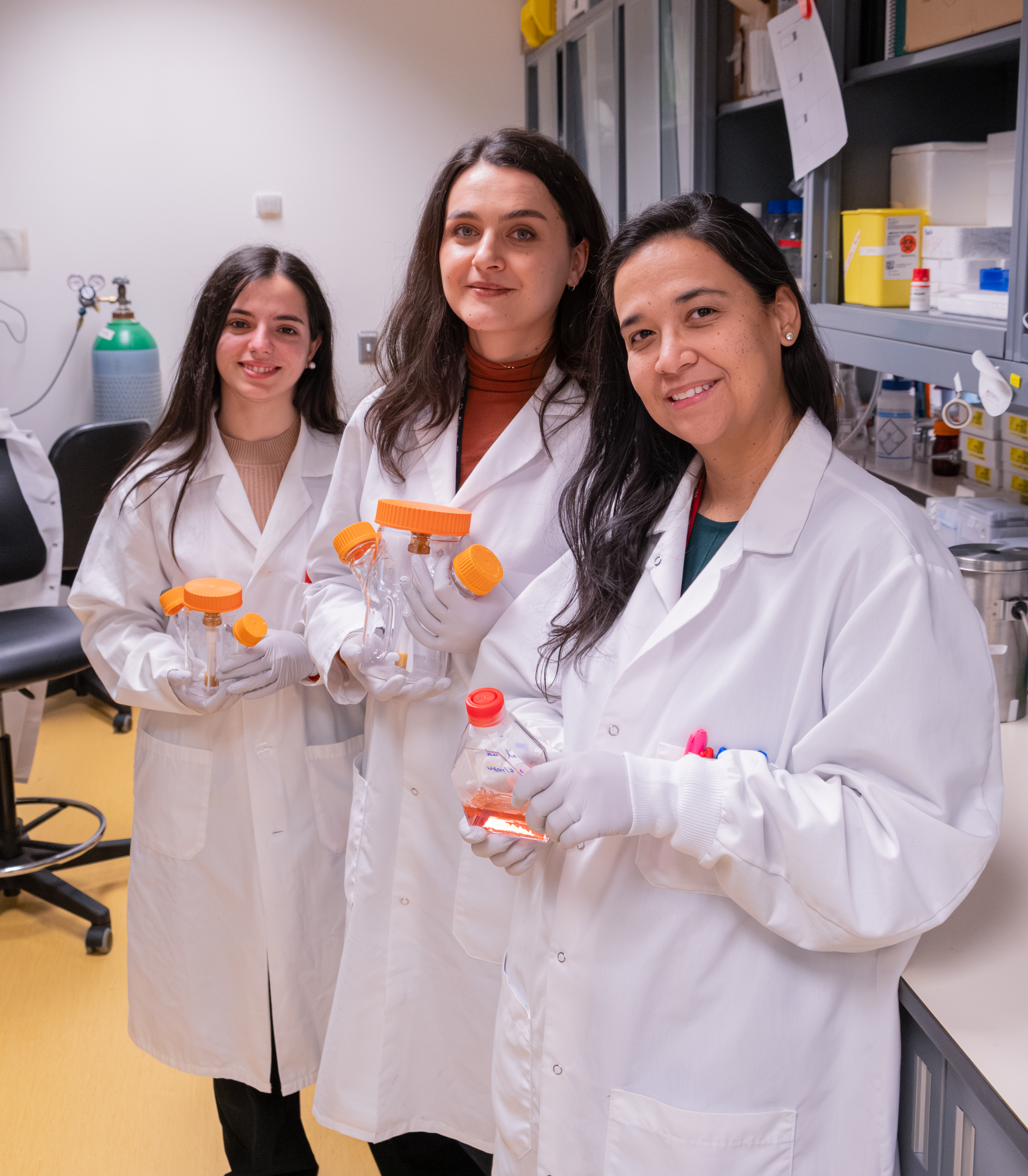Three women in lab coats holding bioreactors. From left to right: Research Assistants María Belén Baeza Trallero and Paula Lépine and Research Associate Cecilia Rocha.