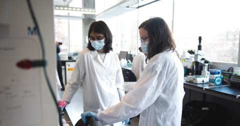 Two women in white coats working in a lab