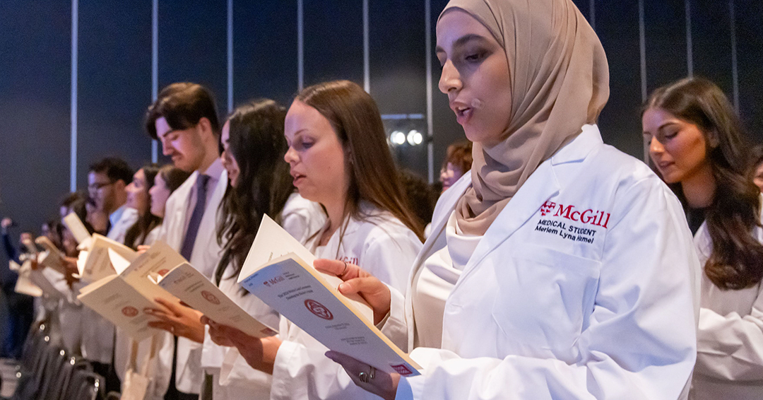 A female medical student wearing a headscarf and a white coat recites the Class pledge at the McGill 2024 White Coat Ceremony