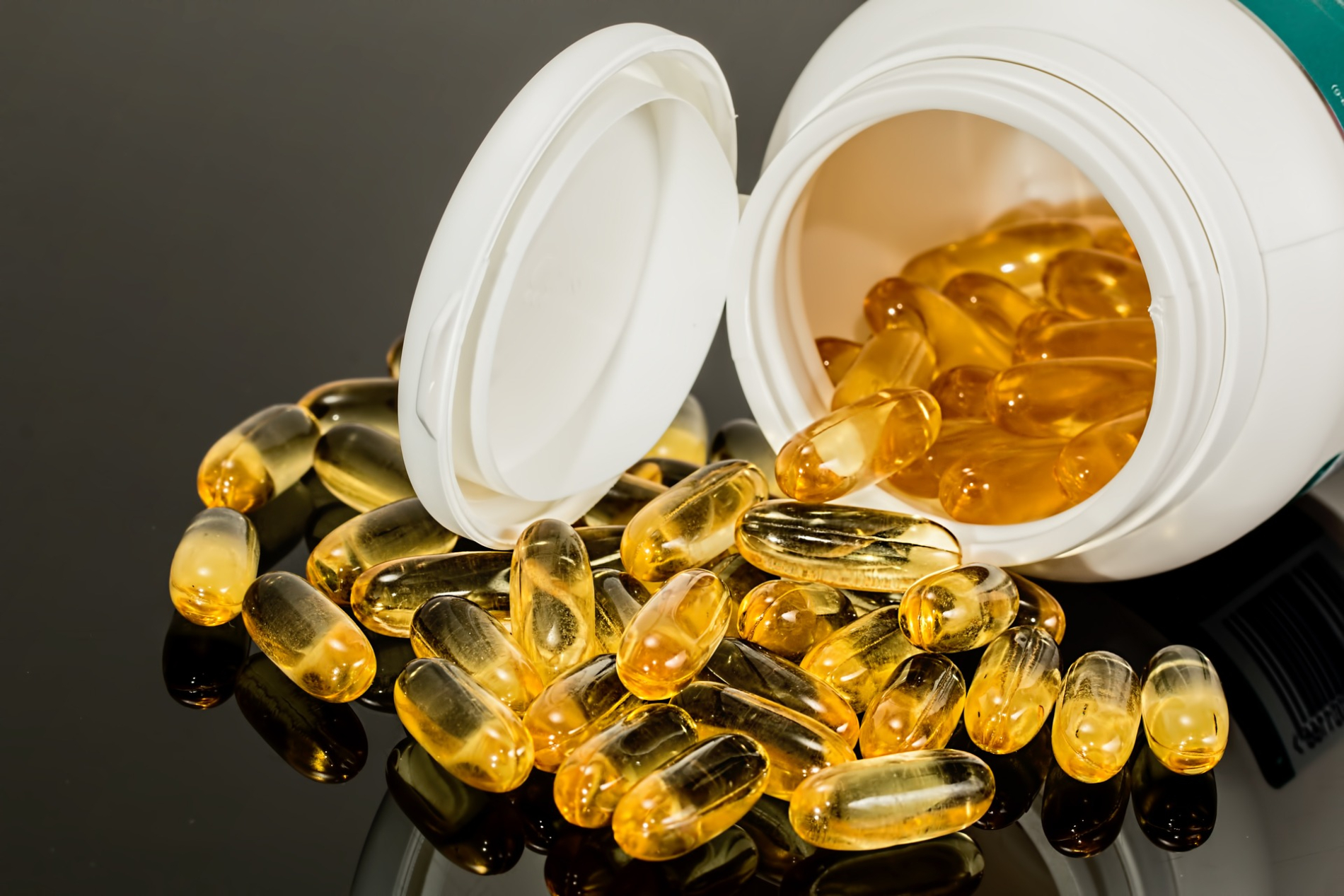 Open bottle from which spill golden gel capsules