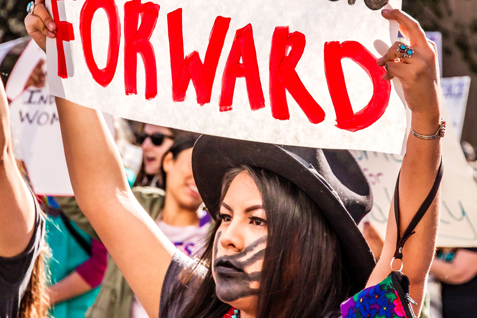 A woman of the Tohono Indian Tribe holds up a sign that reads "Indigenous Womxn will lead us forward" during International Women’s Day March in Tucson, AZ, January 2019. Detail of a photo by Dulcey Lima, Unsplash.com https://unsplash.com/photos/lWLTR81d8oI