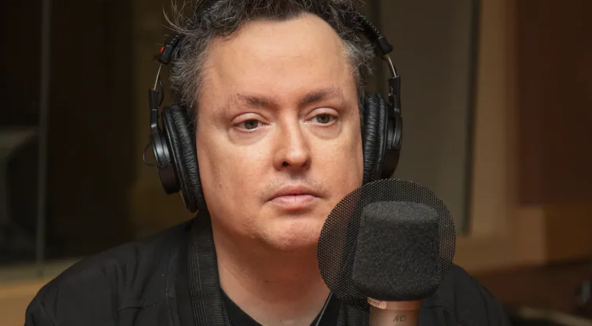Mike Ward wearing headphones sitting in front of a mic 
