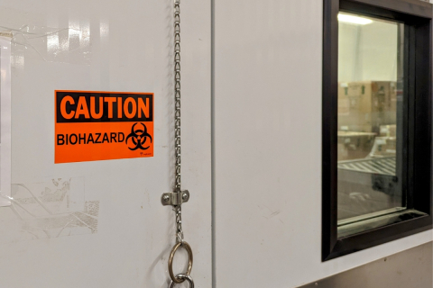 bright orange sticker on a door of a refrigerated room with the text 'caution, biohazard' 