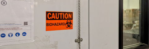 bright orange sticker on a door of a refrigerated room with the text 'caution, biohazard'