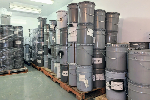 Storage room with a large number of grey steel pails with radioactive waste