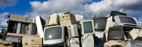 big pile of old computer and TV screens stacked on top of each other outside under a clear sky
