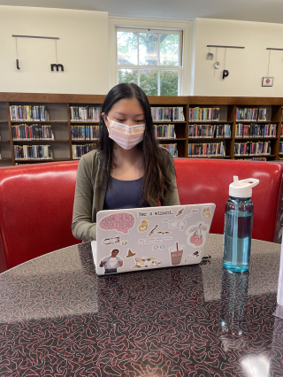Melody, wearing a mask, sitting at a local library with her laptop