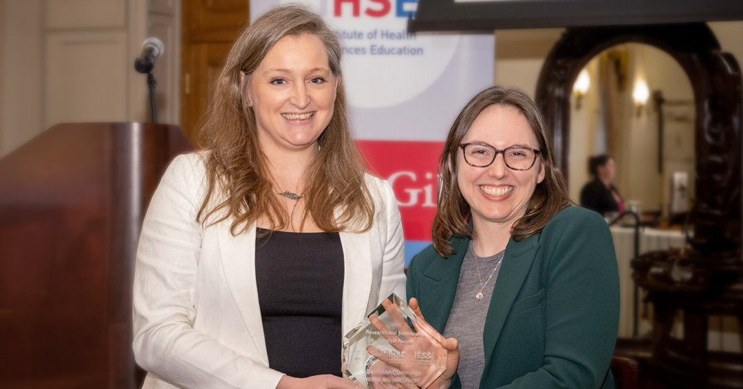 Beth-Ann Cummings smiles at the camera as she receives a glass award from Meredith Young on stage at the McGill Faculty Club 