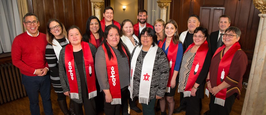 Graduating Indigenous students with red sashes stand with First Peoples' House staff