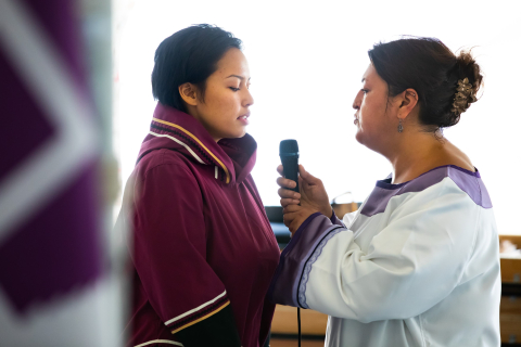 Two women face each other and speak into a microphone