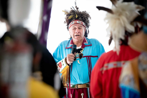 A man in regalia speaking into a microphone at the McGill Powwow
