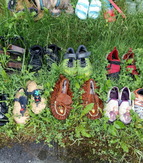Children's shoes, including a pair of moccasins, are arranged in rows on the grass in honour of the children who attended residential schools