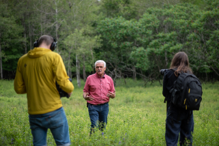 People stand in a field in front of a forest during a medicinal plant walk