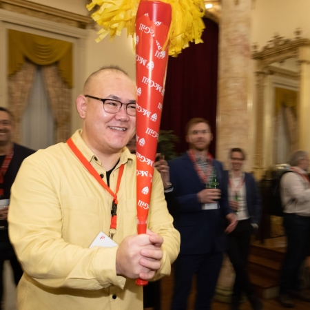 A smiling man holding a plastic torch walking through a crowd of people