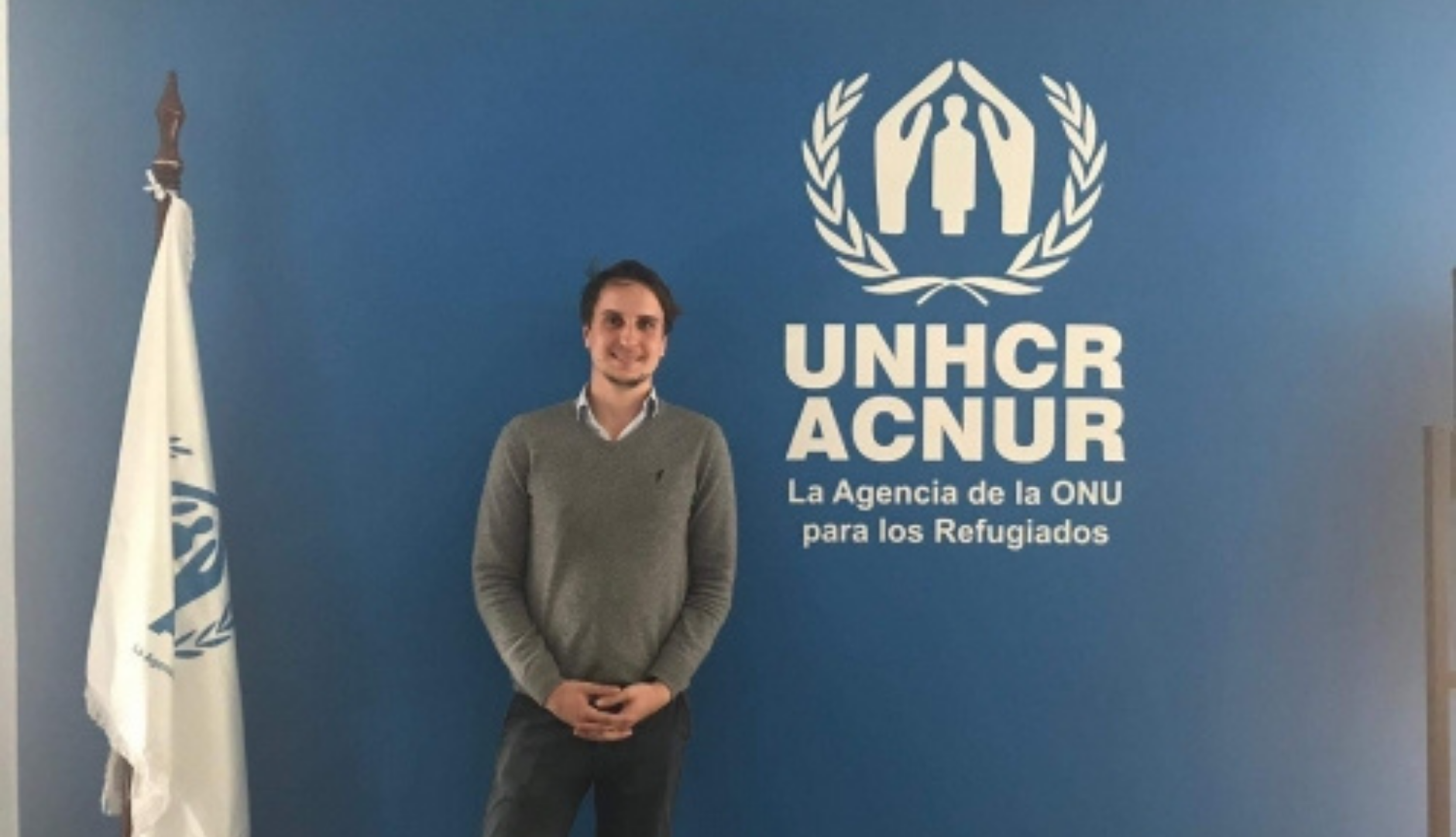 Arthur standing in front of the UNHCR logo