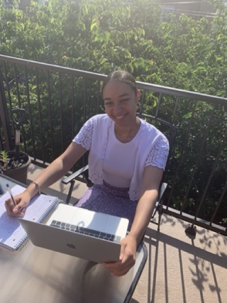 Karlee Thomas working on her laptop, sitting at a table on a balcony on a sunny day