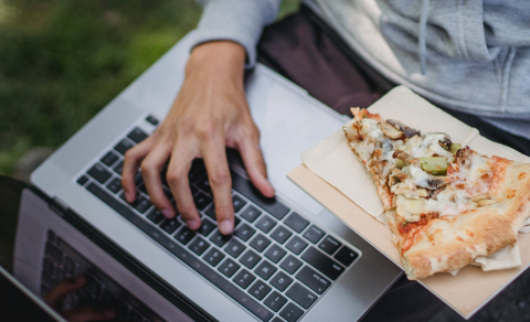 hand on laptop with a slice of pizza on the side