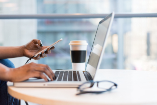 person at laptop computer holding cellphone