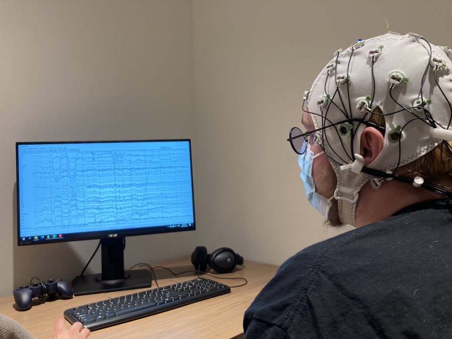 Person with EEG cap looking at computer screen. Computer screen has EEG waves.