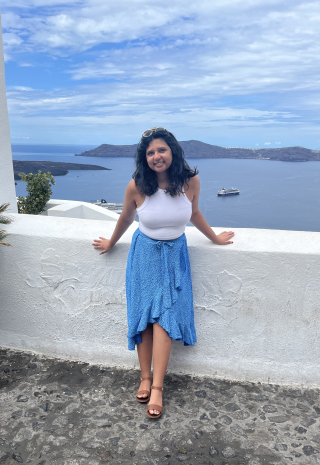 Naima Mansuri leaning against a short white wall, with the ocean in the background.