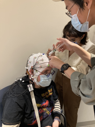 Two students learning how to inject gel into EEG cap. One student is wearing the EEG cap.