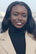 Fanta [A young Black woman,  smiling, standing outdoors, wearing a black turtleneck and a tan coat]