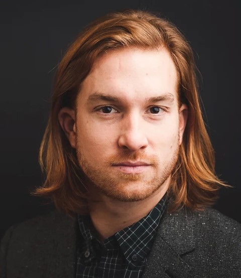 A white man with brown eyes, long ginger hair and a ginger beard. 