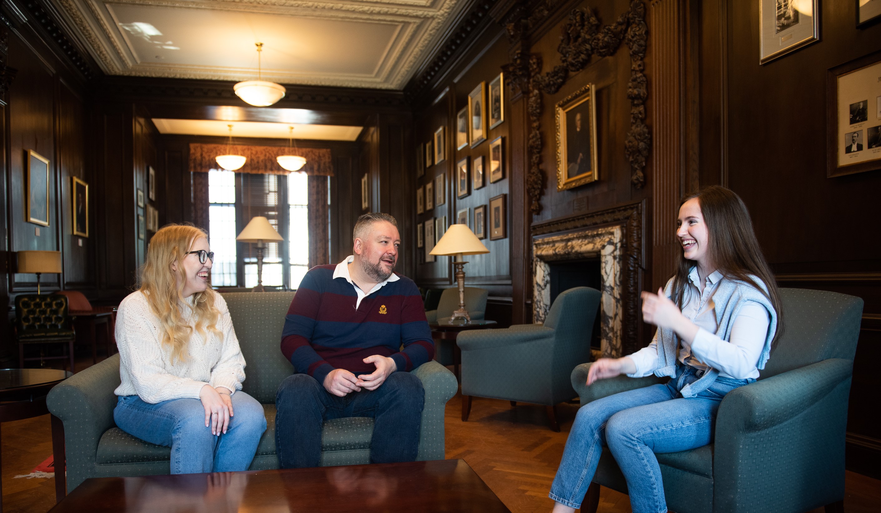 Three white students sitting in the McGill Law common room discussing and smiling. 