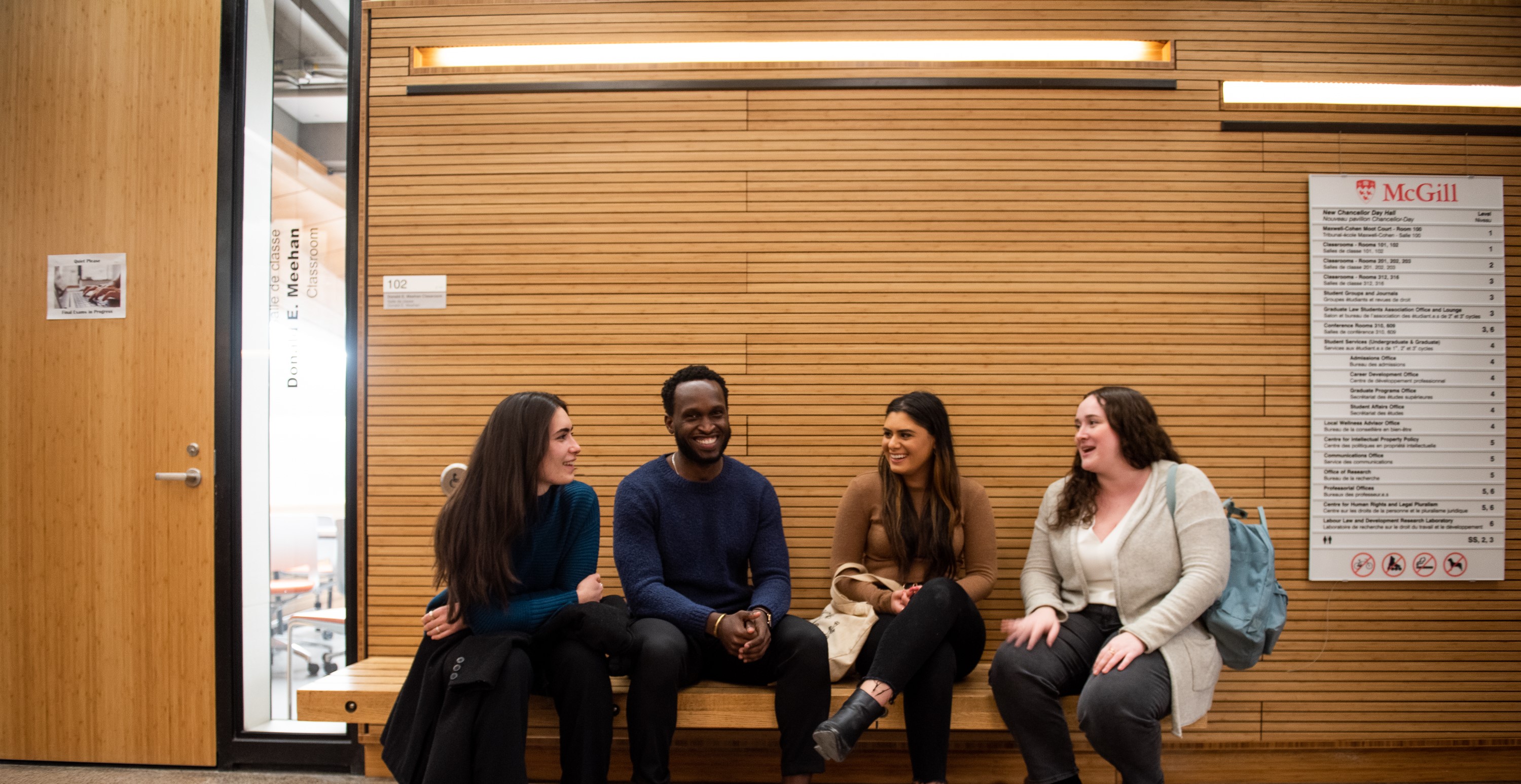 Three white female students and one black male student sitting on a bench discussing and smiling.