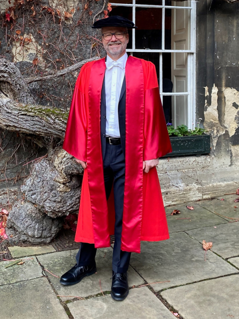 Professor Lionel Smith at Oxford. [A white man wearing red academic robes and a tuxedo stands outside a stone building]
