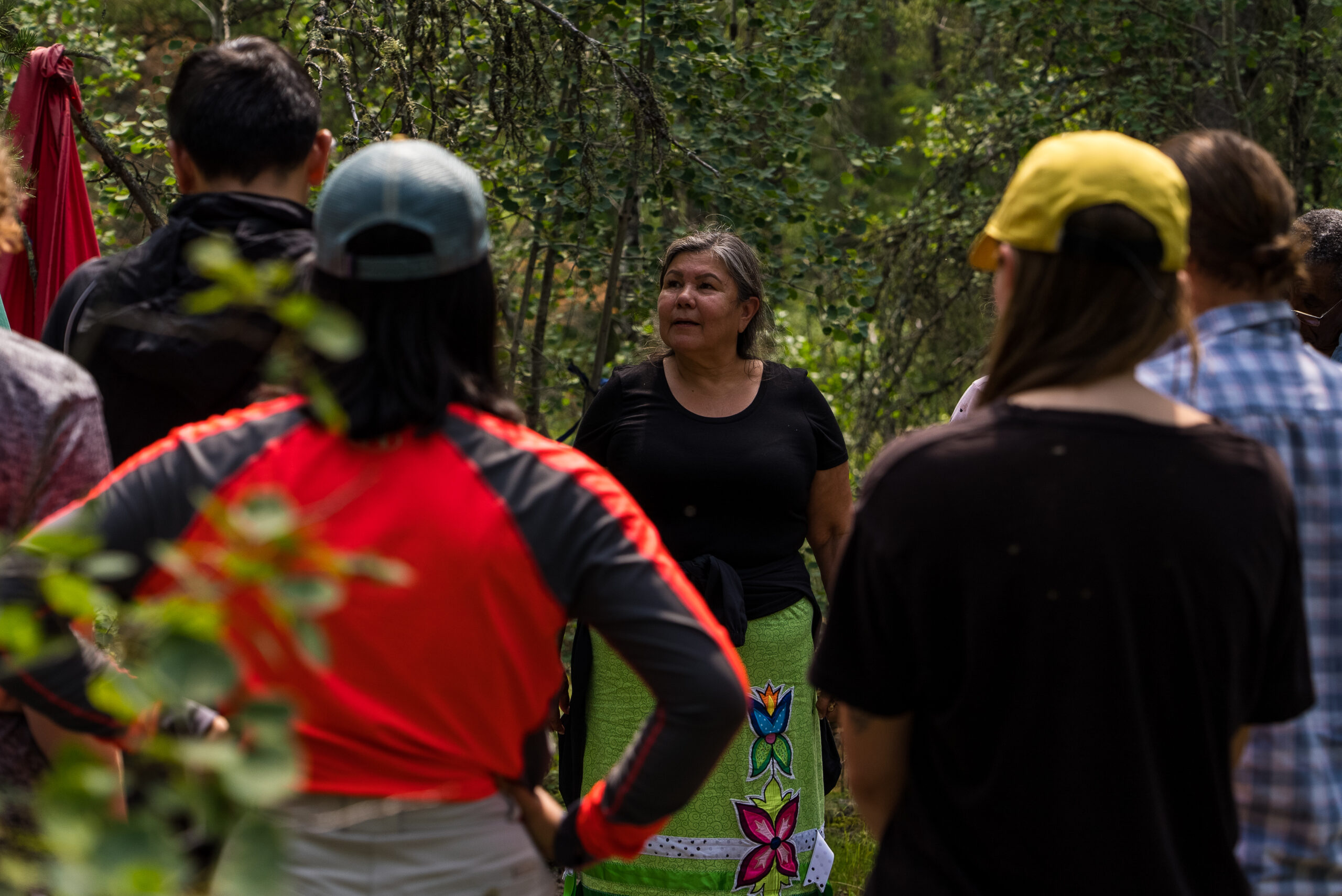 A group of students standing outdoors facing an Indigenous teacher