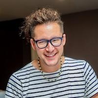Michael David Miller is a smiling man with glasses. He is wearing a striped white and blue shirt.