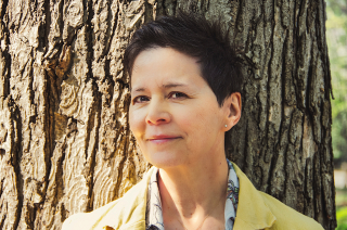 Ann-Marie MacDonald smiling at the camera standing in front of a tree.