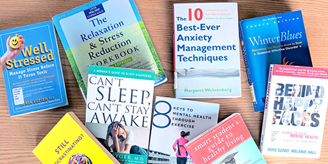 Books on anxiety, sleep and stress reduction seen on a wood table from above.