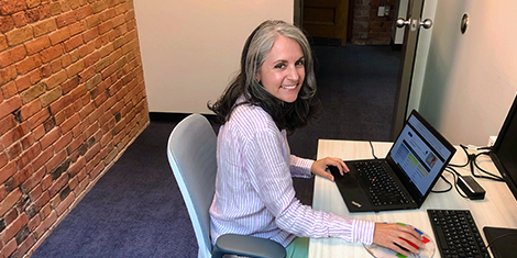 Librarian at desk smiling at camera with exposed brick wall in background.