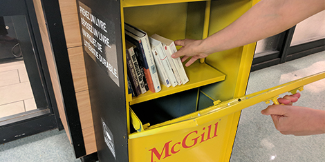 Hand reaching into a Yellow Little Free Library book stand for a book.