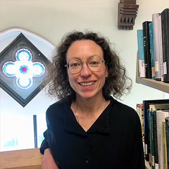 Librarian Anais Salamon smiling at the camera next to a bookshelf with a stained glass window in the background.
