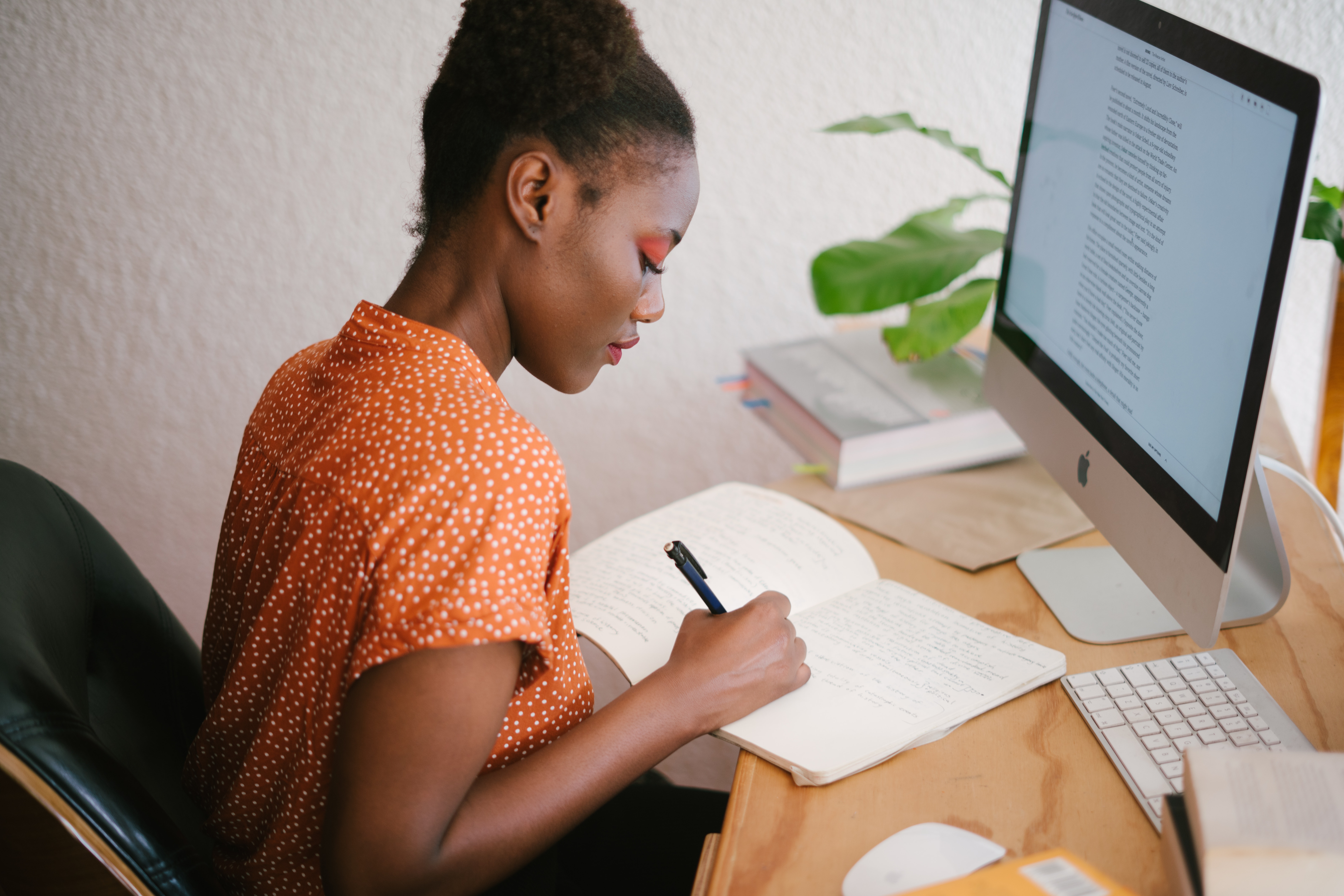 Woman sitting at desk with computer, taking notes.