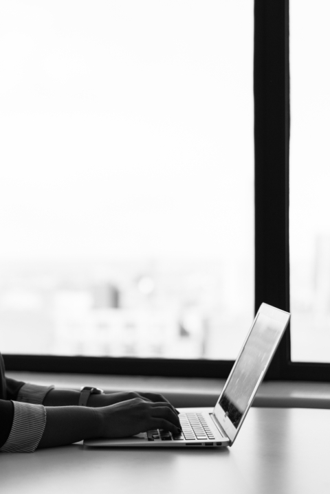 Black and white image featuring hands on a laptop keyboard.