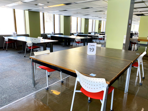 Large open room with multiple tables with numbers on them. Chairs are spaced apart.