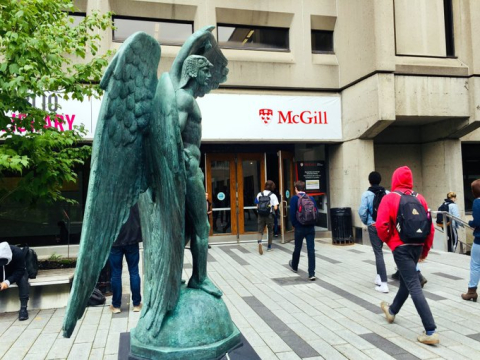 The entrance of the McLennan Library Building with the Falcon statue and students walking through the doors.