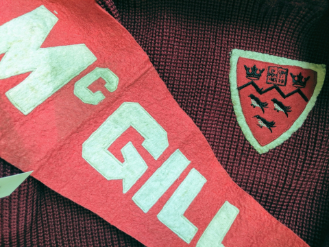 Red archival McGill pennant on top of a vintage McGill hockey sweater featuring a crest.