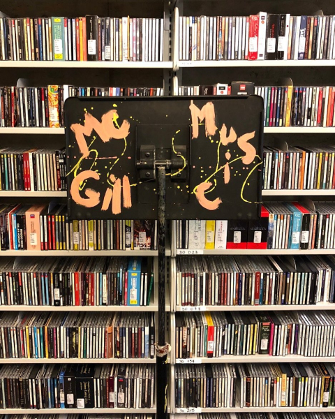 Foreground: music stand with the words "McGill Music" hand painted on it. Background: library stacks filled with CDs.