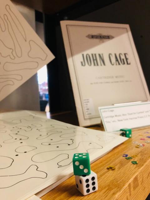 Music / Math exhibit photo of dice in the foreground and John Cage material in the background.