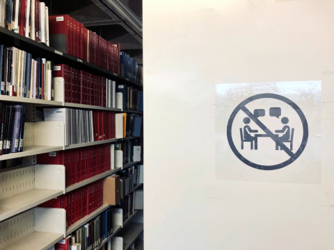 Decal indicating no speaking in foreground with bookshelves in background.