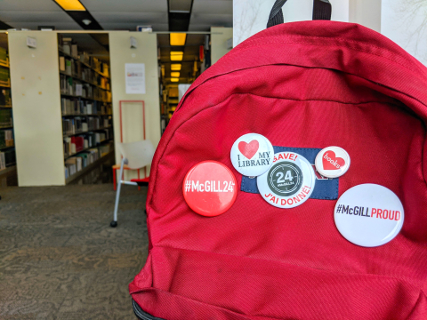 Burgundy back pack with 5 buttons pinned to it with messages saying "I love books" and #McGill24.