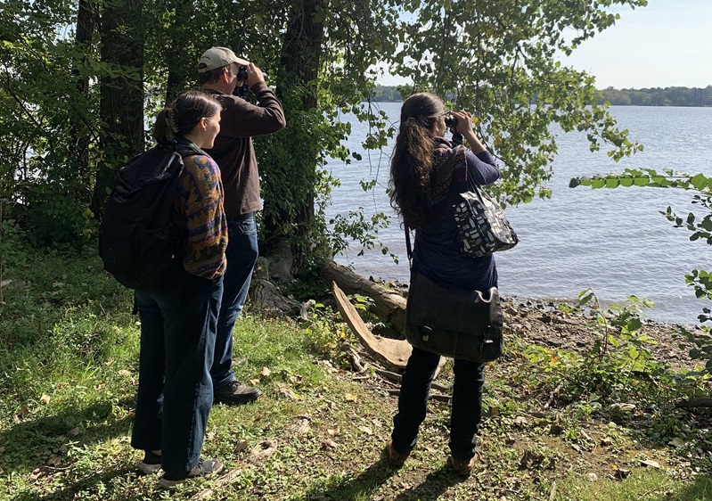 Stduents and professor look out over with water with binoculars