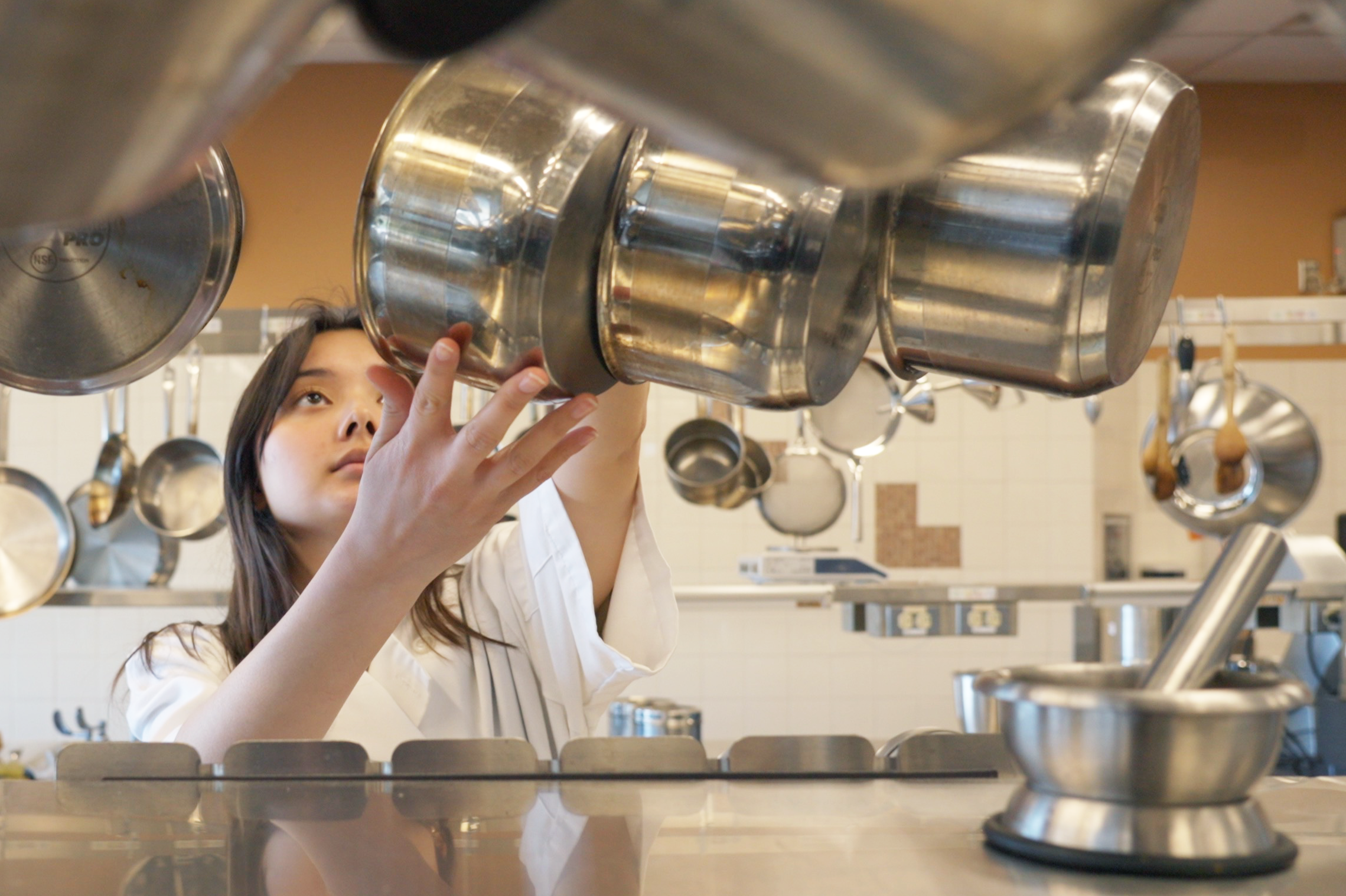 A student in the food lab grabs a pot from a rack